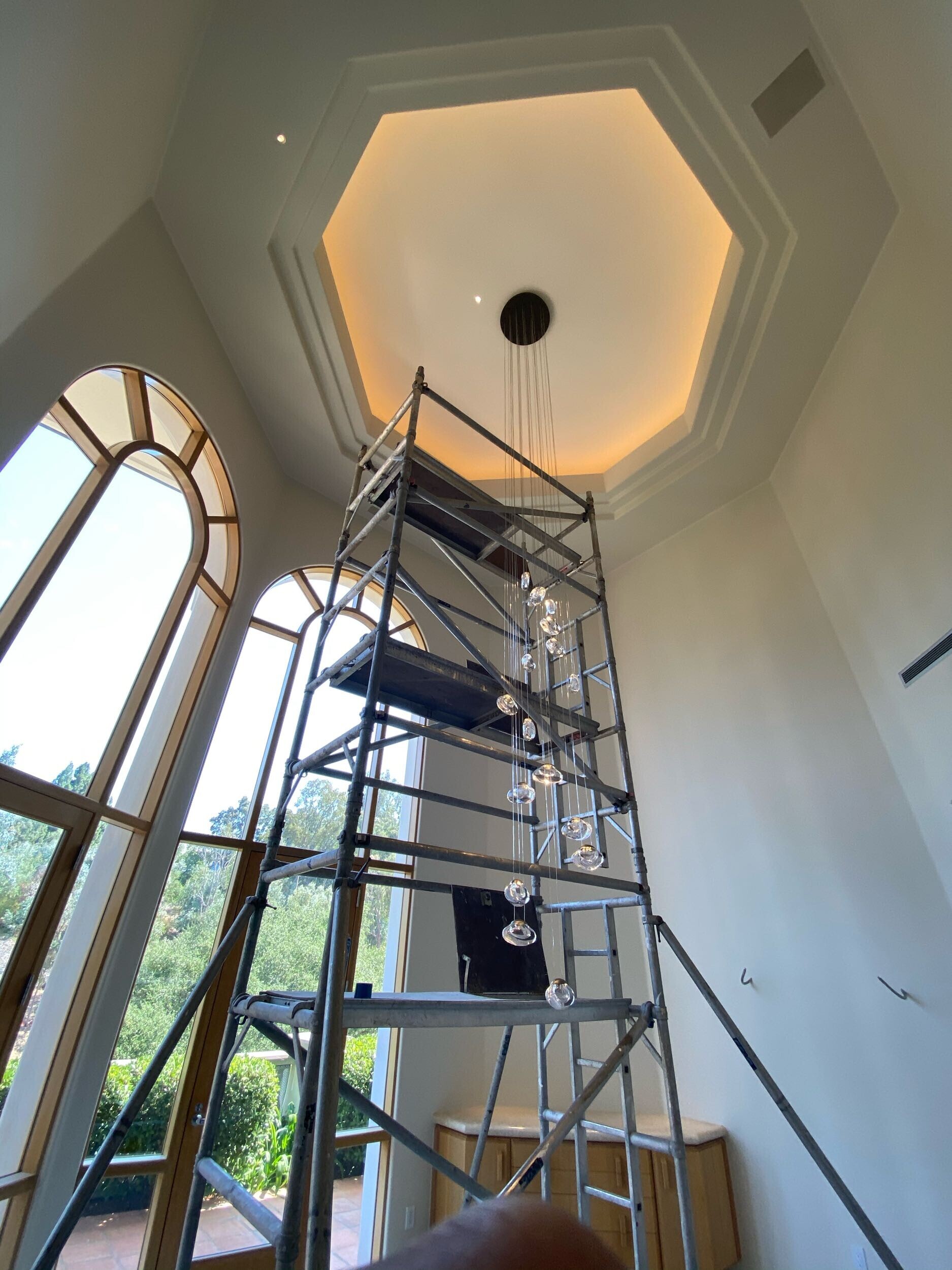 Grand residential sitting room with a large chandelier being mounted by scaffolding. 