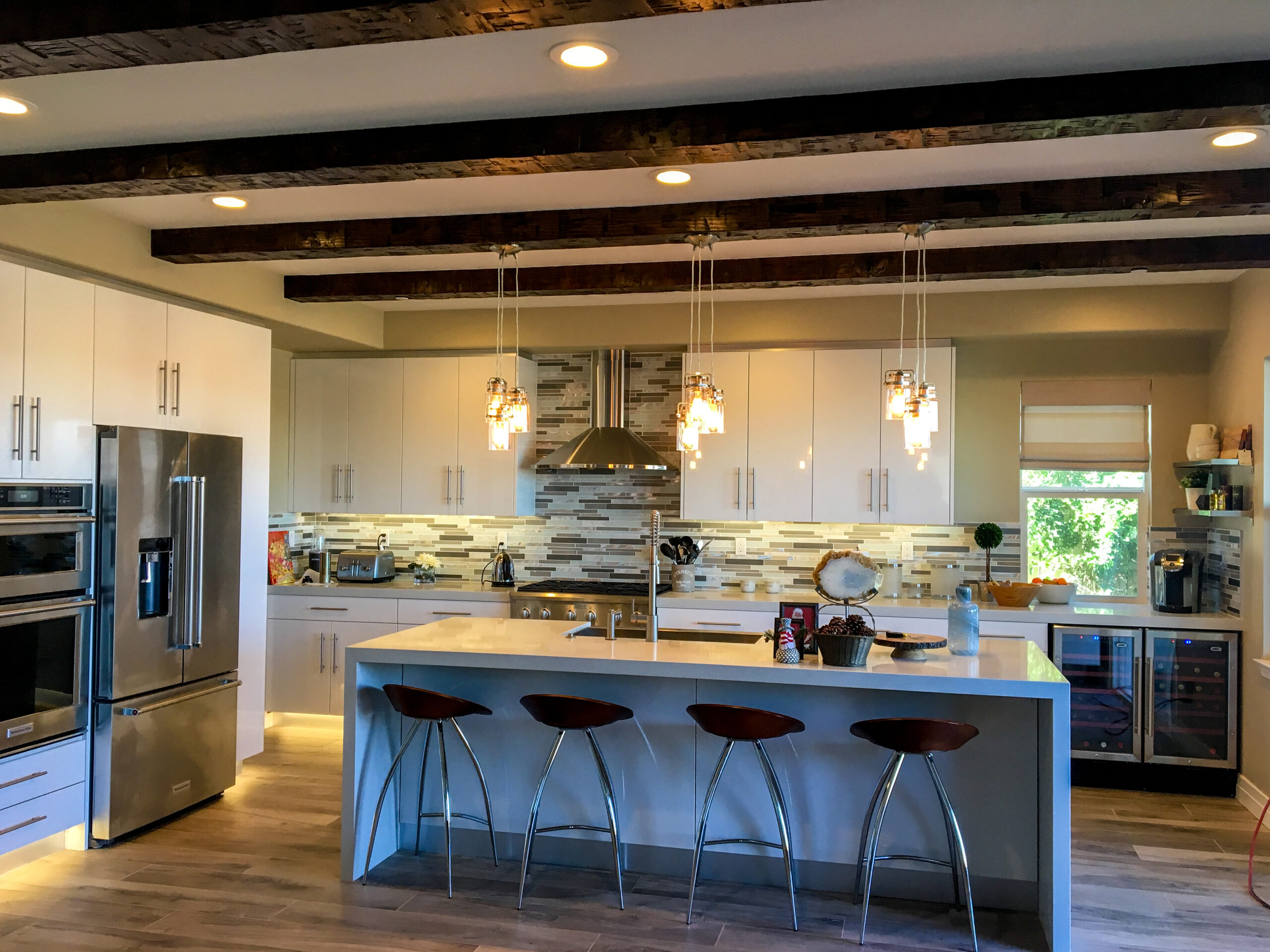 Remodeled residential kitchen with recessed can lighting and three ornate chandeliers hanging above a new granite  countertop